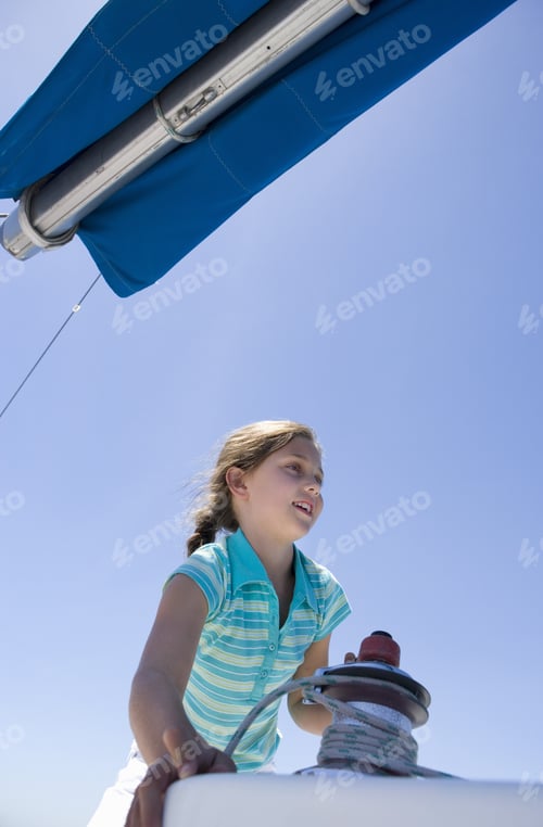 Preview: Girl (8-10) Winding Rope Pulley Of Boat Rigging On Deck Of Sailing Boat Out At Sea, Smiling, Low