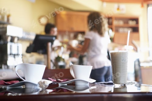 Preview: Waitress Serving Female Customer In Cafe, Focus On Glass And Coffee Cups On Table In Foreground