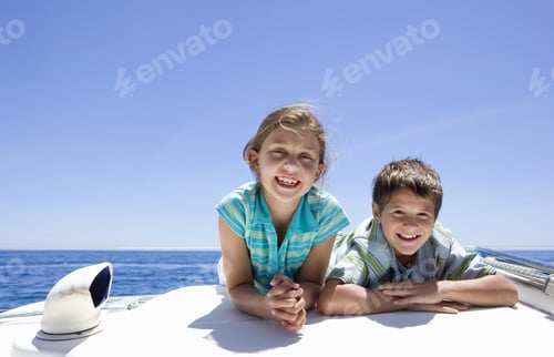Preview: Boy And Girl (8-10) Lying On Front On Deck Of Sailing Boat Out At Sea, Side By Side, Smiling, Front