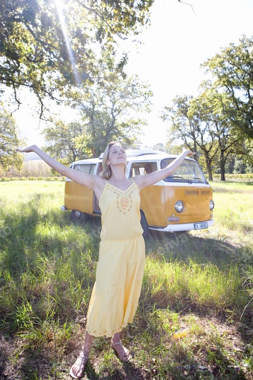 Preview: Young Woman In Field With Arms Outstretched By Camper Van, Eyes Closed (Lens Flare)