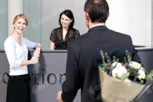 Preview: Businessman With Bouquet Of Flowers Being Greeted By Two Women At Office Reception