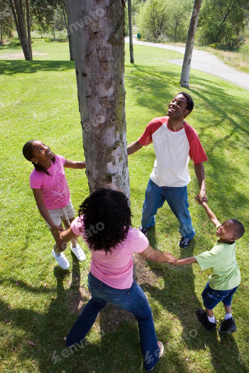 Preview: Family In Circle Around Tree In Park Holding Hands Celebrating Nature And The Environment