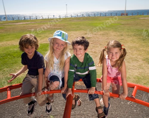 Preview: Four Children Sitting On Outdoor Playground Ride Smiling At Camera