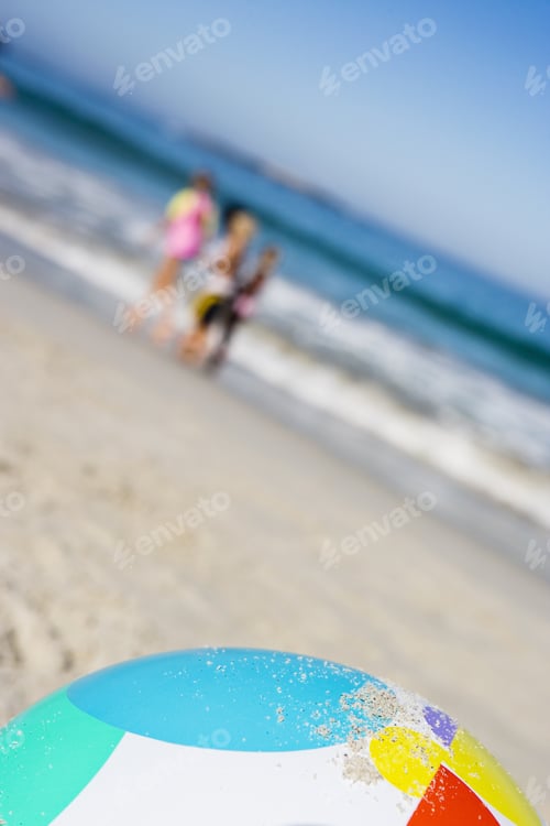 Preview: Children (6-10) Standing On Sandy Beach Near Sea, Focus On Beach Ball In Foreground (Tilt)