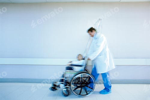 Preview: Doctor Pushing Boy In Wheelchair Along Hospital Corridor With Blur