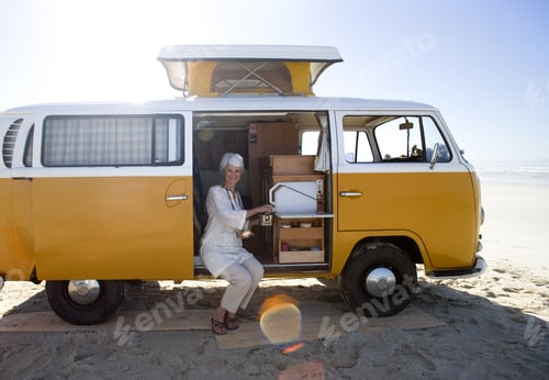 Preview: Senior Woman Making Tea In Camper Van On Beach, Smiling, Portrait (Lens Flare)