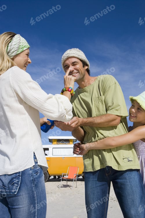 Preview: Family Of Three On Beach, Woman Applying Sunscreen To Man'S Nose, Daughter (5-7) Embracing Father