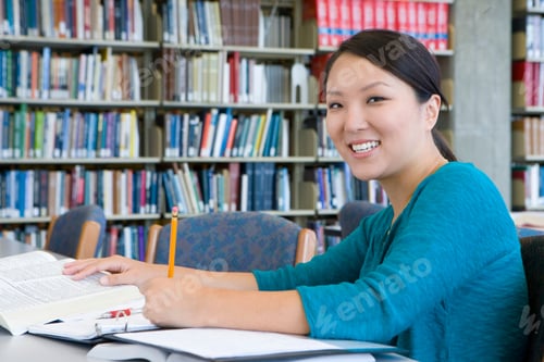 Preview: Female Student Making Notes Studying In Library At Camera