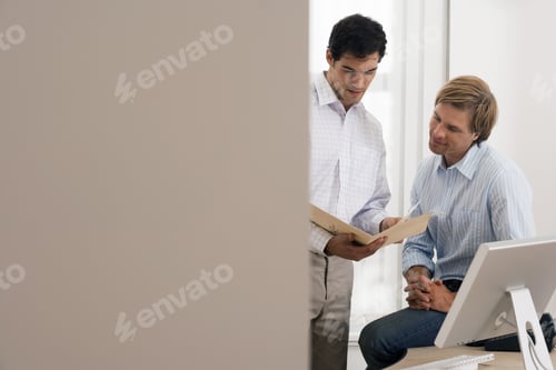 Preview: Two Businessmen Looking At File Beside Desk In Office, Smiling, View Through Doorway