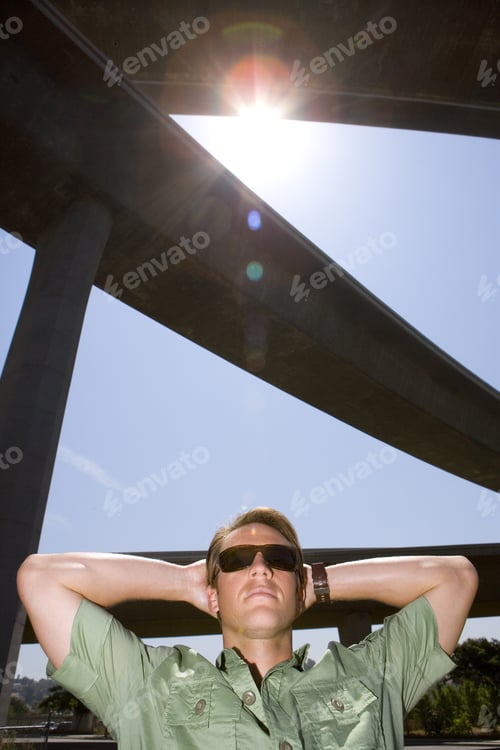 Preview: Young Man With Arms Behind Head Beneath Overpass, Low Angle View (Lens Flare)
