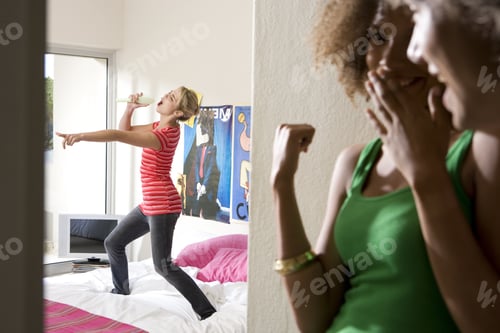 Preview: Two Teenage Girls (15-17) Laughing At Friend Singing In Bedroom