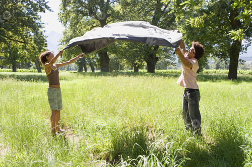 Preview: Young Couple Assembling Tent On Camping Trip In Woodland Clearing, Side View