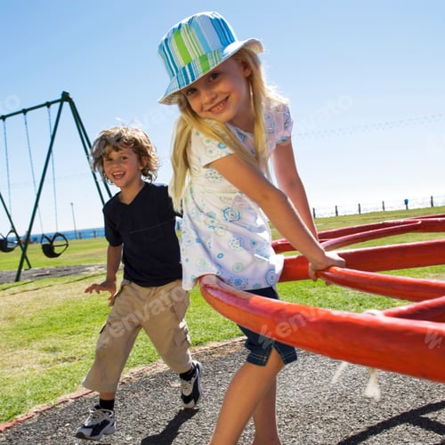 Preview: Two Young Children Having Fun Playing On Playground Roundabout Smiling At Camera