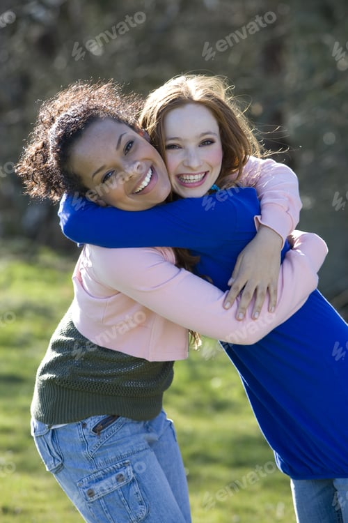 Two Young Women Embracing and Smiling Outdoors