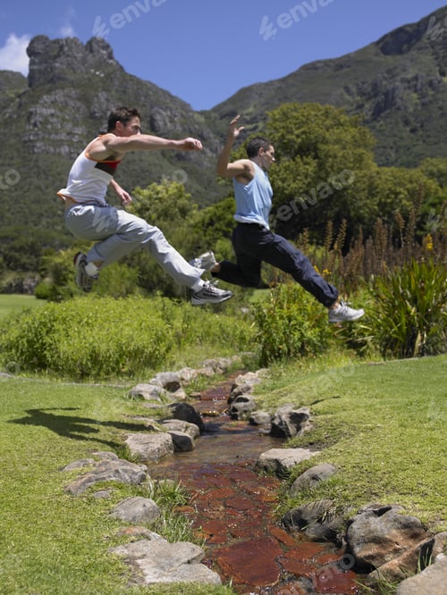 Preview: Side Profile Of Two Young Men Jumping Over A Stream