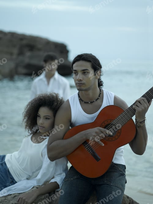 Preview: Young Man Playing The Guitar With A Young Woman Looking Away