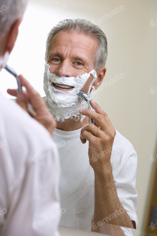 Preview: Senior Man Shaving At Home, Using Razor And Shaving Foam, Reflection In Bathroom Mirror, Smiling