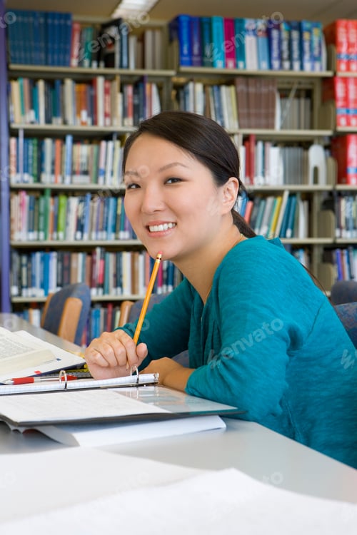 Preview: Female Student Making Notes Studying In Library At Camera