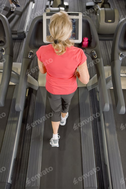 Preview: Senior Woman Running On Treadmill In Health Club