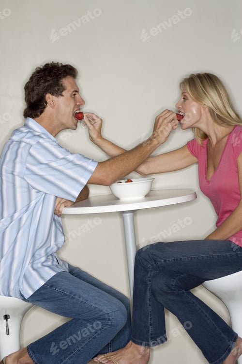 Preview: Couple Sitting At Table In Kitchen, Feeding Each Other Strawberries, Face To Face, Smiling, Profile