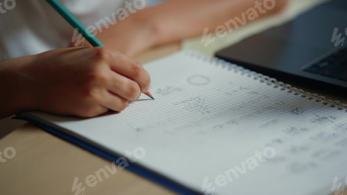Preview: Closeup Boy Hand Writing In Notebook Next To Computer At Table. Unknown Schoolboy Solving Math