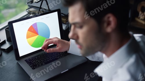 Preview: Serious Businessman Working On Laptop Computer At Home Office. Male Freelancer Pointing At Graphs