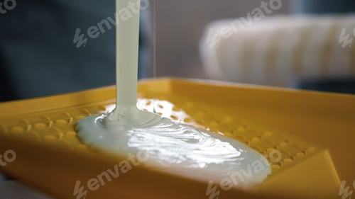 Preview: White Paint For Walls Decoration Pouring To Plastic Tray Indoors. Dye Spreading In Yellow Container