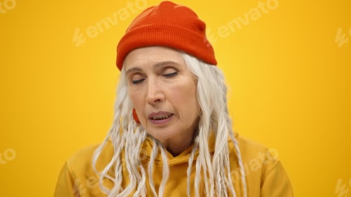 Preview: Old Happy Woman Telling Funny Story On Yellow Studio Background. Cheerful Elderly Lady Posing To