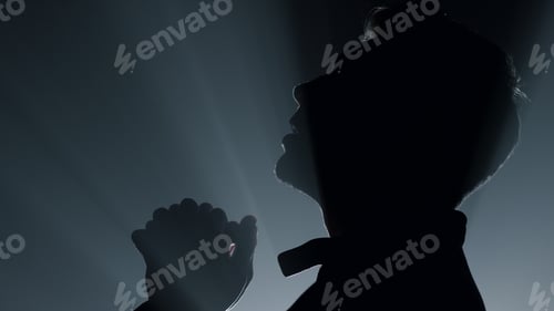 Preview: Silhouette Of Religious Man Saying Prayer In Darkness. Young Male Person Praying In Spotlights