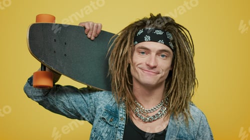 Preview: Portrait Of Stylish Man Holding Skateboard On Shoulder In Studio. Closeup Smiling Skateboarder