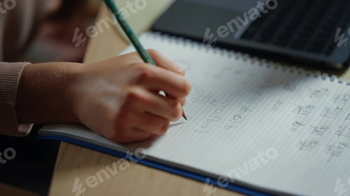 Preview: Closeup Girl Hand Writing In Notebook Next To Computer At Table. Unknown Student Solving Math