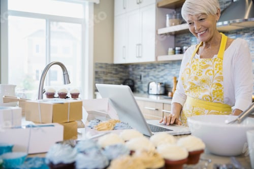 Preview: Woman With Laptop Baking Cupcakes In Kitchen