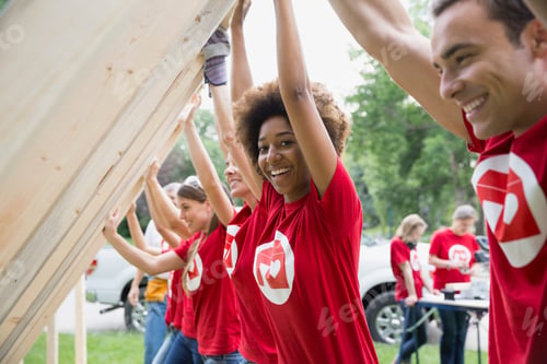Preview: Portrait Of Smiling Volunteers Lifting Construction Frame