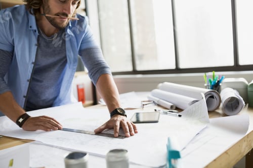 Preview: Architect Drafting Blueprints At Table