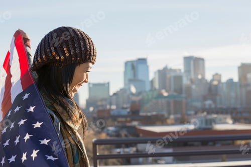 Preview: Cheerful Woman Holding American Flag Against Cityscape