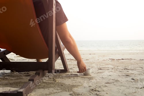 Visualização: Homem sentado na cadeira na praia com a mão segurando o café da manhã