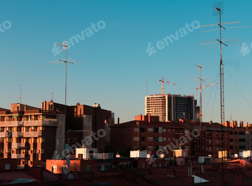Preview: A City Under A Clear Gradient Blue Sky During Sunset With Television Antennas On Building Roofs