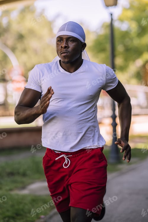 Preview: A Vertical Shot Of An African-American Male In A White Shirt Jogging At The Park During Daytime