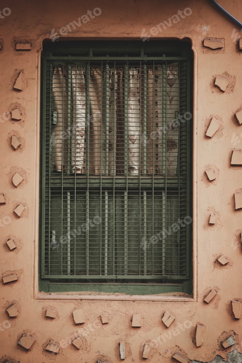 Preview: A Vertical Shot Of A Soft Pink House Wall With Stone Pieces Glued Around The Green Bars Of A Window