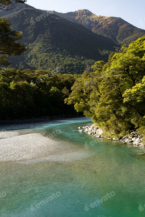 Preview: A Vertical Picture Of A River Surrounded By Hills Covered In Forests Under The Sunlight
