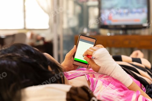 Preview: Senior Patient Hand Injured With Bandage Lying Down And Using Cell Phone.