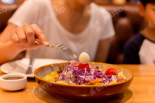 Preview: Woman Hand With Fork Eating Salad With Tomato And Quail Egg In A Plate.