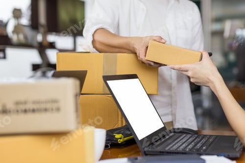 Preview: Man Giving Parcel Boxes To Woman With Open Laptop On Table