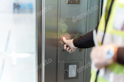 Preview: Security Man Hand In Protective Glove Against Covid-19 Pressing Lift Buttton