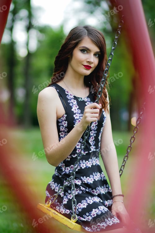 Preview: A Vertical Portrait Of A Young Female Posing On A Swing In A Park
