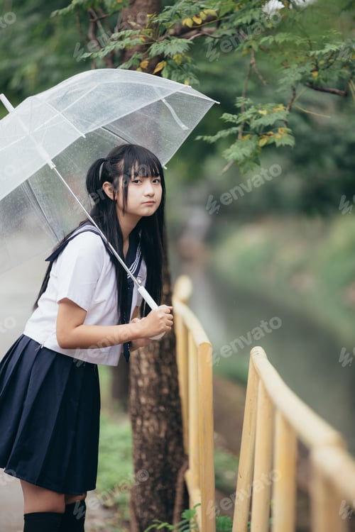 Preview: Portrait Of Asian School Girl Walking With Umbrella At Nature Walkway On Raining