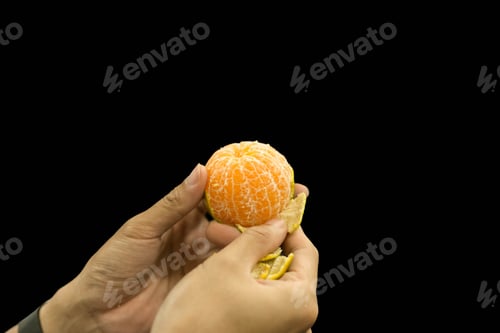 Preview: Hand Peeling Orange Fruit Isolated In Black Background