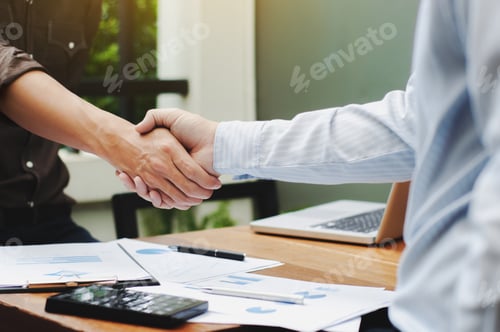 Preview: Close-Up Of Two Business Executives Shaking Hands With Data Documents On The Table