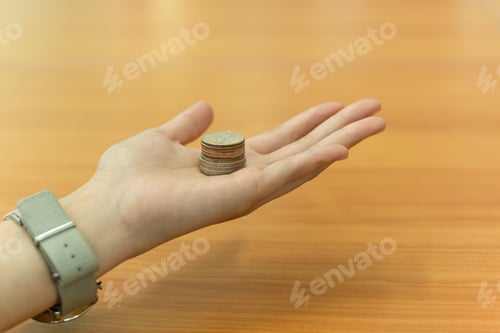 Preview: Open Hand Holding Thia Coin On Wooden Table In Background.