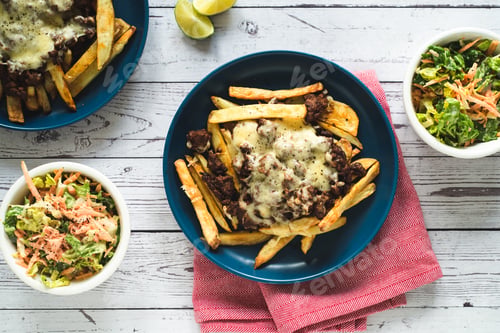 Preview: A High Angle Shot Of Servings Of French Fries With Fried Meat And Cheese, Salads In Bowls, And Limes